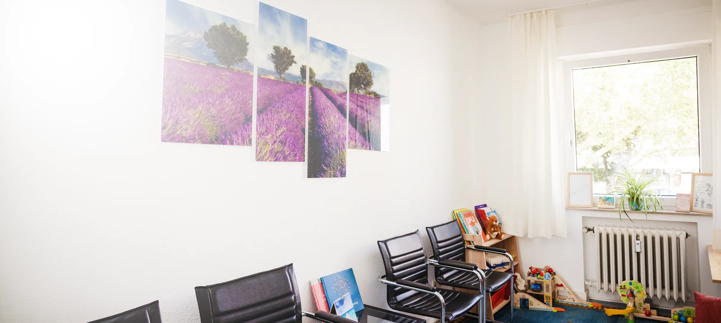 Wartezimmer der Praxis mit Lavendel-Wandbildern und Spielecke